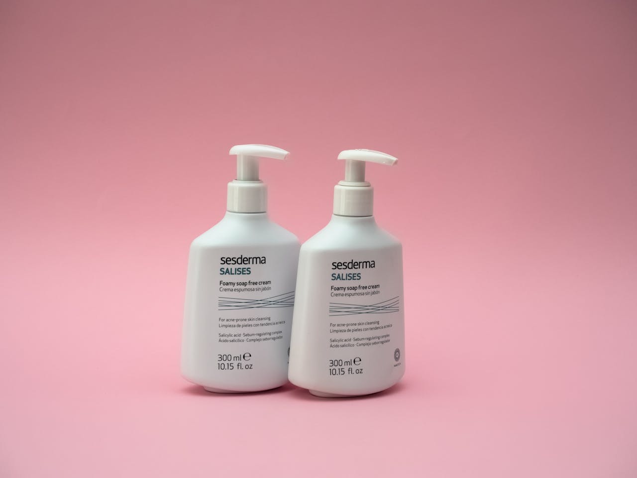 Two bottles of Sesderma Salises foaming cream against a pink backdrop.